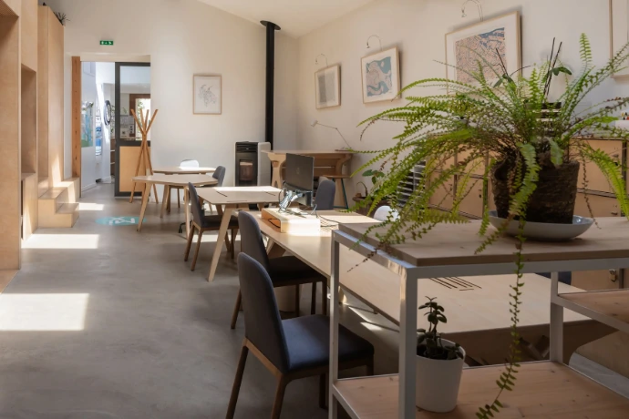 Open space du MIX Coworking, grand espace avec velux et haute hauteur sous plafond, poêle, plantes et casier le long des murs. Plusieurs tables en bois avec chaises en tissus confortables.