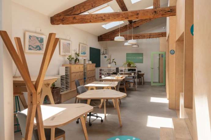 Open space du MIX Coworking, large pièce avec poutre et grande hauteur sous plafonds, plusieurs tables en bois avec chaises et porte manteau