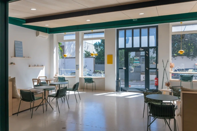 Open space du MIX Café, large baie fenêtres et portes vitrées donnnant sur la rue, pièce très spacieuse et lumineuse avec des chaises de café vertes avec tables en bois