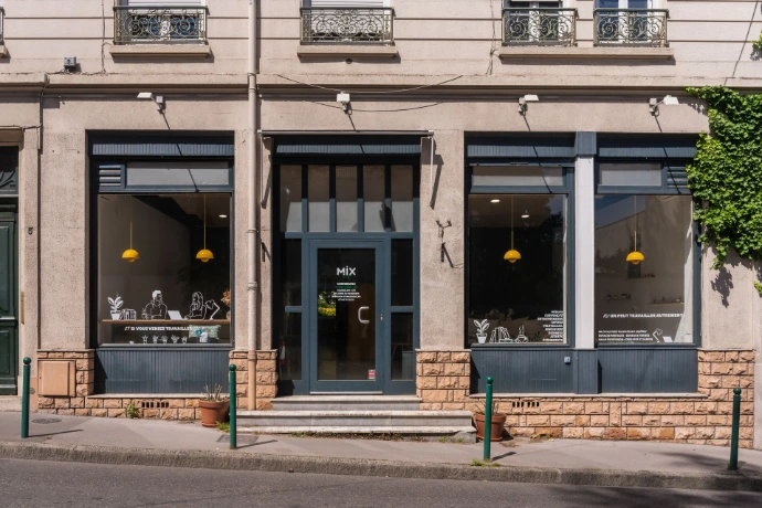 Facade du MIX Café vu de la rue d'en face, larges fenêtres bleu pétroles avec touche de jaune à l'intérieur, espace ensoleillé