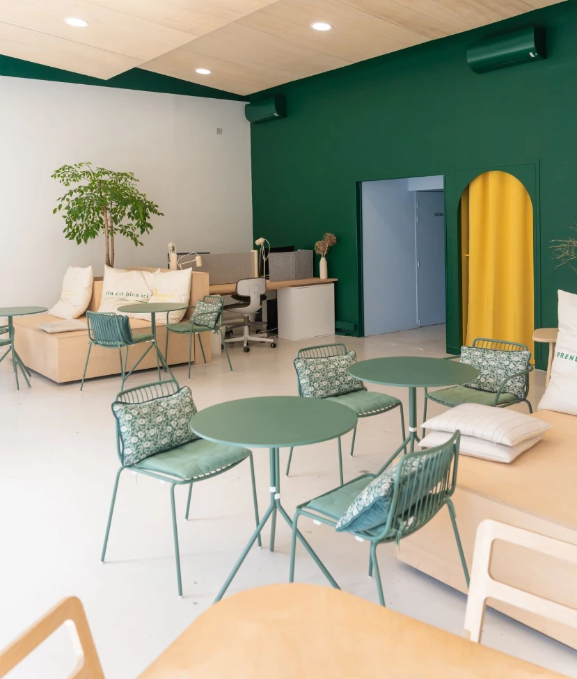 Open space du MIX Café vu d'un coin, plan proche sur les tables et chaises, vue du mur en face de la porte vert avec fond bleu.