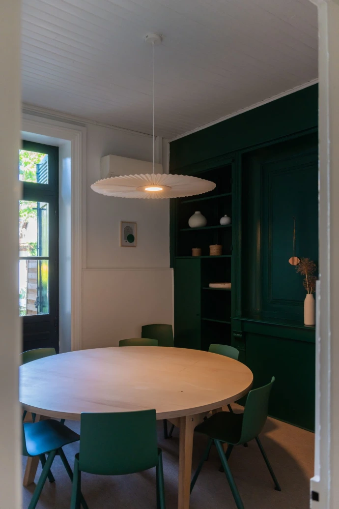 Salle de réunion Le Jardin Vert vu de la porte d'entrée, table ronde en bois massif avec chaises vertes autour, avec grande fenêtre donnant sur le jardin.