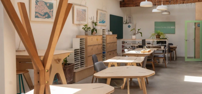 Open space du MIX Coworking, large pièce avec poutre et grande hauteur sous plafonds, plusieurs tables en bois avec chaises et porte manteau